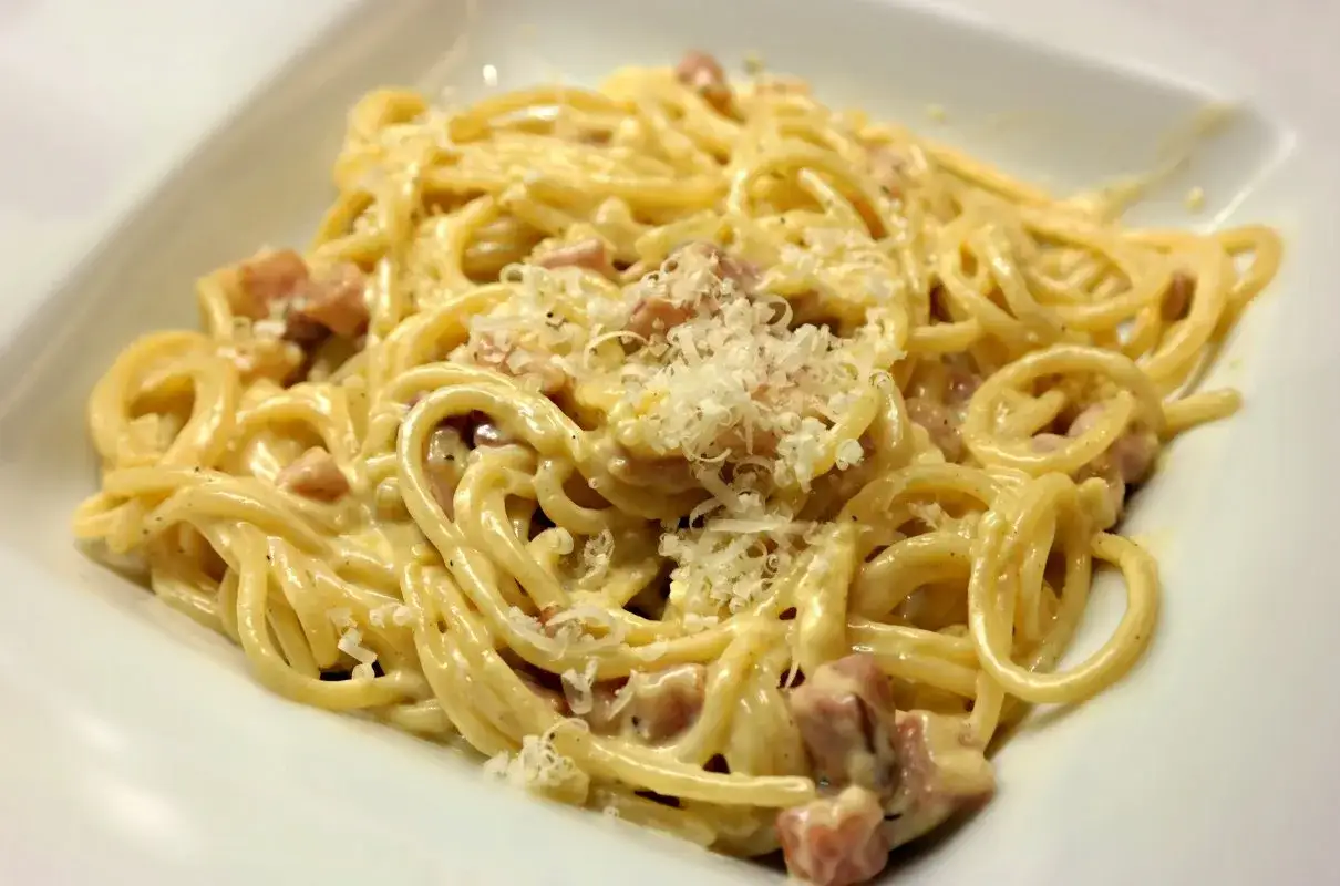 Pyszna carbonara z boczkiem, podana w białej misce, posypana startym parmezanem.